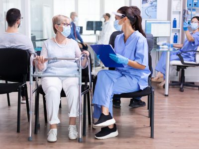 handicapped-senior-woman-with-walking-frame-hospital-waiting-room-using-walking-frame-talking-with-medical-staff-about-treament-illness-coronavirus-pandemic